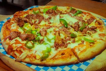 flank steak pizza with peppers, onion and extra gratin cheese Mexican style on a wooden platform in a restaurant