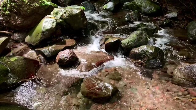 clear mountain water flowing in a river over rocks, sunlight shining on the flowing river water, recording with the original sound of gurgling water.