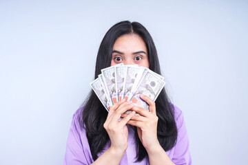 Asian business woman hiding behind bunch of money banknotes on grey background