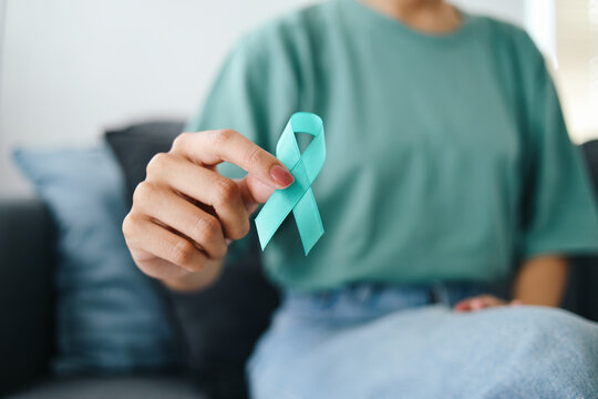 Close-up teal awareness ribbon holded by woman hands to support cancer survivor. Ovarian Cancer month, cervical cancer day.