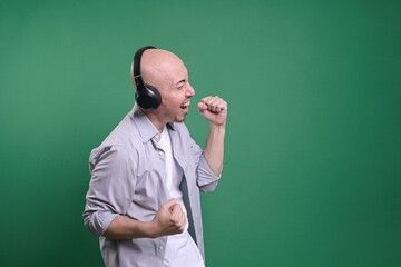 Side view of bald man listening music with headphones and clenching fist making victory gesture