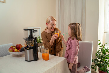 Mother and daughter drinking raw, cold pressed juice in the kitchen, health conscious 