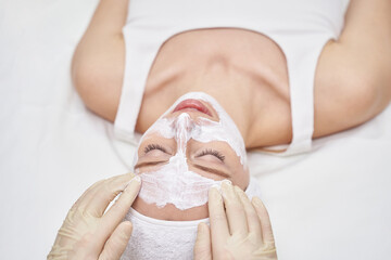 In spa studio, young woman enjoys a facial treatment. A beautician applies a white clay mask, promoting skincare and wellness. She lies down, embracing relaxation and femininity