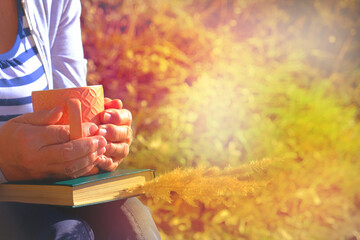 Pensive elderly senior woman with a cup of coffee or tea outdoors on a sunny day in autumn, reading a book