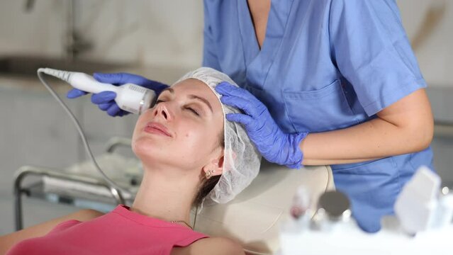 Adult woman cosmetologist performs hardware facial whitening procedure to young female patient