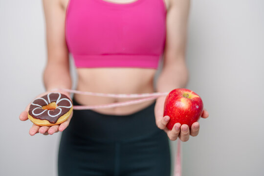 woman hand hold red Apple and donut, female fitness choose between fruit is Healthy and sweet is Unhealthy junk food. Dieting control, Weight loss, Obesity, eating lifestyle and nutrition concept