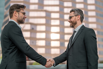 Two businessmen shaking hands on city street. Business men in suit shaking hands outdoors. Handshake between two businessmen. Handshake with partner in the city for greeting, dealing, merger.