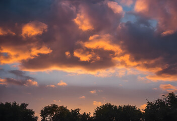 Obraz premium Dramatic sunset sky with fiery clouds over silhouette of trees.