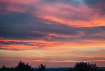 Dramatic sunset sky with vibrant orange and pink clouds over a silhouette of trees.