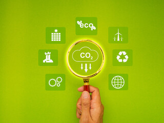 Hand holding a magnifying glass with a CO2 icon over a green background.