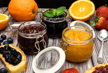 Glass jars with different types of jam on wooden table. Homemade orange, strawberry and blueberry marmalade