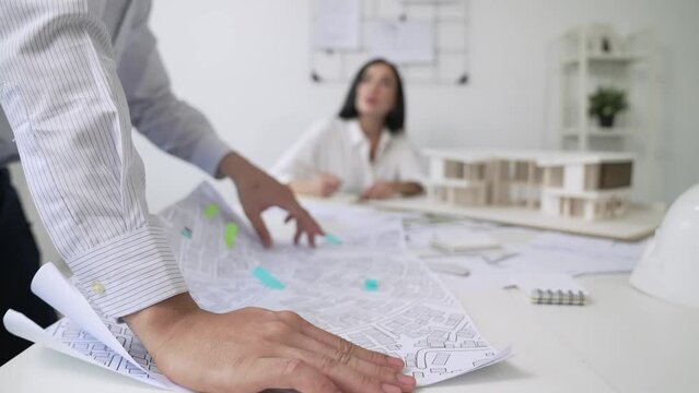 Skilled caucasian interior designer working with house model while discussing with asian architect engineer about house plan on meeting table with blueprint and house model scatter around. Immaculate.