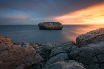Fototapeta na wymiar Warm sunrise in Islares with a close-up of rocks and a rock in the middle of the sea
