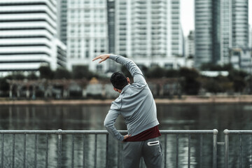 A man stretching his muscle  in the city center park before  cardio workout, running.  Health and Lifestyle in big city life concept. - obrazy, fototapety, plakaty