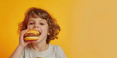 Foto auf Acrylglas portrait of a kid eating delicious hamburger on color background, copy space © Kien