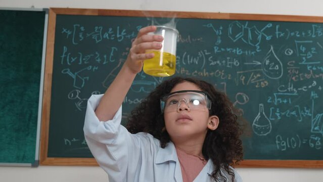 Attractive american student hold beaker and inspect biochemical solution. Close up of curious girl stirring beaker and looking at color changing while standing at laboratory with blackboard. Pedagogy.