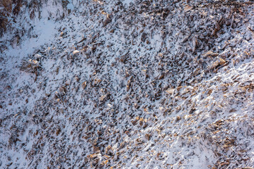 Frozen ice rockies close-up. Natural texture of snow-covered frozen stony rocky wall. Ascetic snowy background with rocks and stones in high altitude. Cold nature backdrop of mountain on great height.
