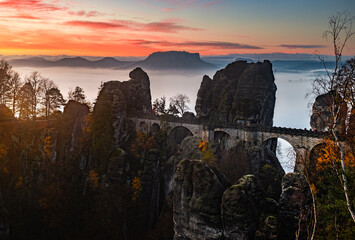 Saxon, Germany - The Bastei bridge on a sunny sunrise with colorful morning sky, autumn foliage and heavy fog under the hill. Bastei is famous for the beautiful rock formation in Saxon Switzerland Nat