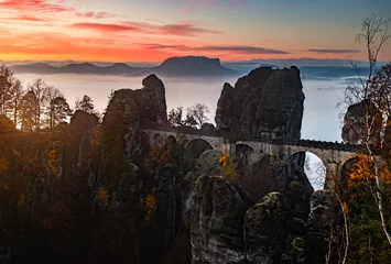 Wall murals Bastei Bridge Saxon, Germany - The Bastei bridge on a sunny sunrise with colorful morning sky, autumn foliage and heavy fog under the hill. Bastei is famous for the beautiful rock formation in Saxon Switzerland Nat