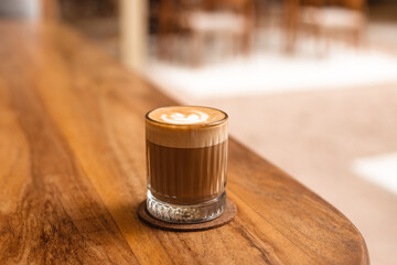 Cappuccino in a glass on a wooden table, side view. The concept of delicious selected coffee.
