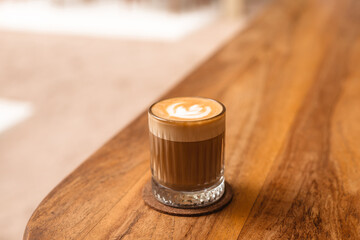 Cappuccino in a glass on a wooden table. A stylish concept for a coffee shop and bean roasters. Delicious coffee with butter milk