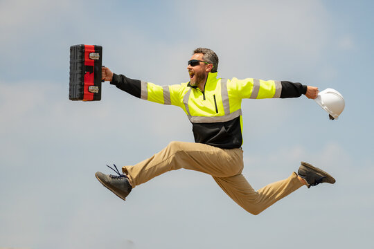 Crazy builder excited jump on site construction. Excited builder construction worker in a safety helmet jumping in front of the trucks. Excited crazy builder man in helmet jump outdoor.