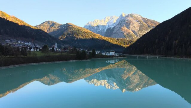 Lake with crystal cear water surrounded by mountains and a small town in Bellluno, Italy.