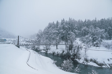 真っ白な雪で覆われた、川と吊り橋の風景