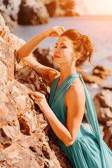 Woman green dress sea. Woman in a long mint dress posing on a beach with rocks on sunny day. Girl on the nature on blue sky background.