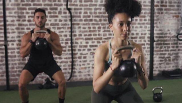 Man, woman and kettlebell squat at exercise class or weight lifting cardio, health body or fitness workout. Training partners, sweat and power group in club for wellness sports, together or challenge