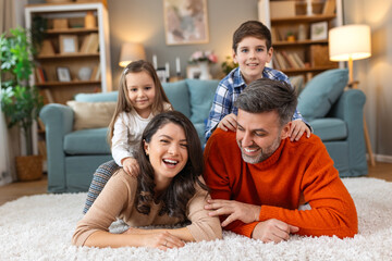 Happy parents and their small kids talking while lying on carpet at home.
