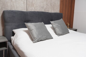 hotel bed with grey pillows and clean white linen with a grey headboard