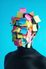 A studio portrait of a woman in front of a blue background with various postits covering her face as a symbol of burnout and excessive demands at work.
