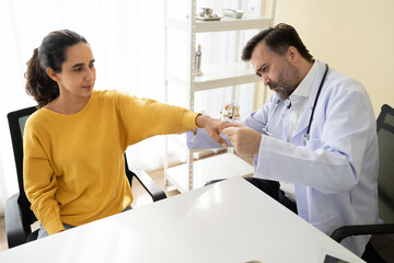 Patient Latin woman meeting Caucasian doctor and doctor checking her arm or hand at hospital	