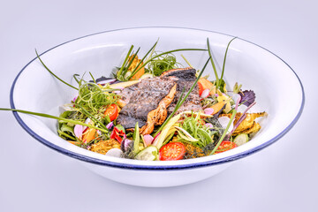 Fresh garden salad with grilled fish filets on top in a white bowl