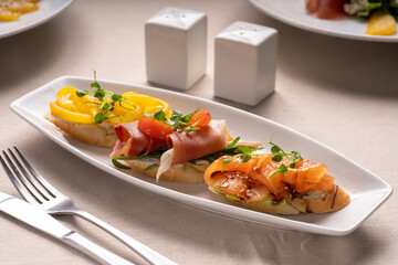 Plate of assorted Italian appetizer bruschetta with chopped salmon, jamon and pepper on ciabatta bread, garnished with tomatoes and microgreen
