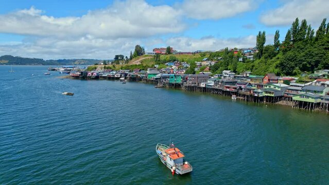 Colorful castro stilt houses on chiloe island with a boat cruising, aerial view