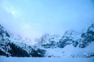 Winter dawn in mountains. Beautiful winter landscape with mountain lake and snowy hills. Morskie oko lake. Lake in tatra mountains in winter at dawn. Poland, Zakopane.