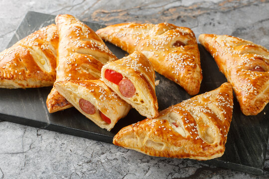 Puff pastry Pigs in a blanket pies with sausage, cheese, sesame and pepper close-up on a marble board on the table. Horizontal