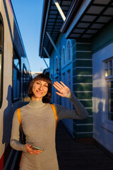 A young traveler with a phone in her hands stands on the platform and says goodbye, waving to someone on the train. say goodbye before leaving.