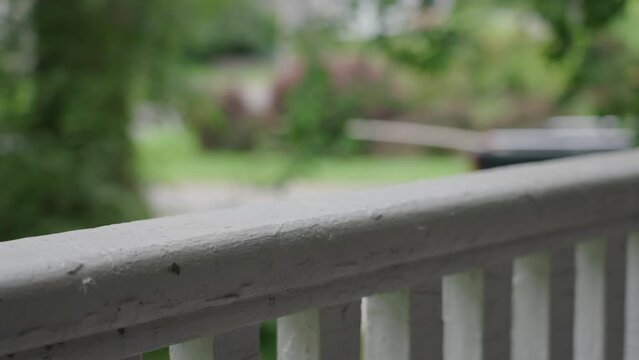 An old white veranda railing with several layers of paint in focus in the foreground, with trees and a black truck passing on the road in the distance, on a summer day