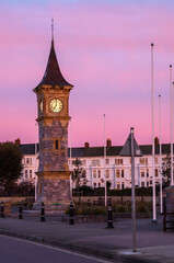 A clock tower along the seafront at dawn, early morning pink sky cast over the buildings. Sweeper...