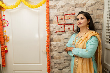 Happy young indian woman standing in her new house with swastik red color in background wall. Griha Pravesh Concept - obrazy, fototapety, plakaty