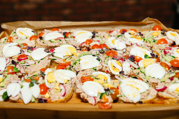 Freshly Prepared Open Sandwiches with Toppings. A tray of open sandwiches with a variety of toppings including eggs, tuna, cherry tomatoes, and fresh vegetables, ready to be served.