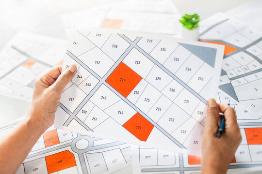 Woman holding a cadastral map looking at lots of lands. Land plot management - real estate concept with vacant land for building construction and housing subdivision for sale, rent, buy, or investment