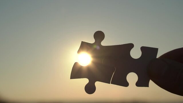 Puzzle pieces are connected. Puzzle pieces in hand on a sunny sky background. Business, partner, solution, alliance, union concept. 