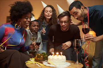 Portrait of adult man using wheelchair and blowing candles on Birthday cake with group of friends celebrating at home