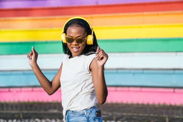 Joyful afro woman with headphones dances against a vibrant LGBT color backdrop.