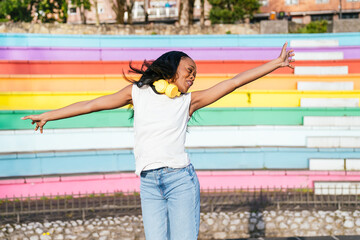 Carefree afro woman with headphones enjoys a moment of freedom by a pride wall.