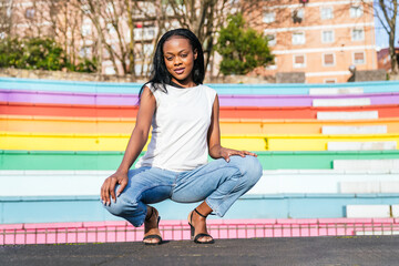 Stylish woman crouching confidently with a rainbow backdrop.